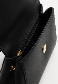 Černá crossbody taška z texturované kůže, která má zipovou kapsu a zlaté kovové detaily s předním zacvakávacím uzávěrem.