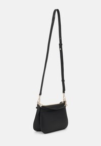 Fekete bőrből készült keresztpántos táska állítható pánttal, arany színű fémrészletekkel és dupla cipzáras rekeszekkel fehér háttérrel.