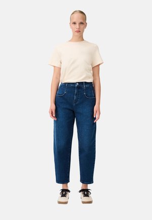 Lichtbeige katoenen t-shirt met korte mouwen, gecombineerd met donkerblauwe denim high-waisted jeans met voorzakken. Zwarte en crèmekleurige veterschoenen.