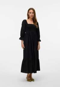 Robe noire avec un décolleté carré, corsage smocké et manches longues bouffantes. Elle présente un ourlet froncé et est fabriquée en tissu léger.