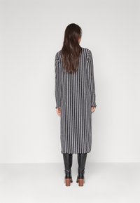 Robe longue rayée avec des lignes verticales noires et blanches, texture tricotée et manches longues, associée à des bottes noires à talons hauts.