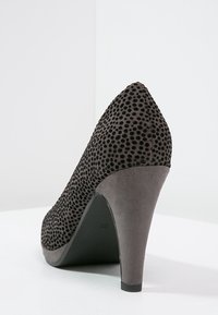 Escarpin noir à talon haut avec un dessus en polka dot texturé, bout pointu et un talon gris lisse. Le matériau semble doux et velouté.