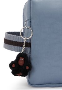 Borsa sintetica blu chiaro con una tracolla a strisce nere e marroni. Presenta un portachiavi a forma di gorilla morbido e peloso attaccato tramite un anello argentato.