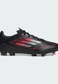 Bottines de football noires avec une tige synthétique texturée et des accents rouges, un design épuré et des crampons proéminents pour une traction sur les surfaces herbeuses.