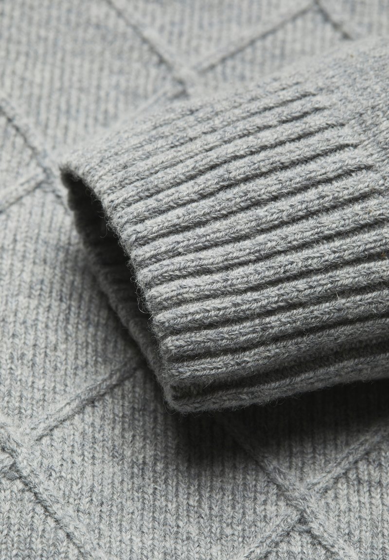 Grauer gestrickter Pullover mit einem strukturierten Diamantmuster und gerippten Bündchen. Das Material wirkt weich und gemütlich, mit unterschiedlichen Stoffbreiten.
