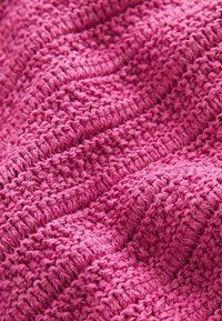 Strukturierter Strickstoff in lebhaftem Pink mit erhabenen Mustern und unterschiedlichen Stichen, die ein wellenförmiges Erscheinungsbild und eine taktile Qualität erzeugen.