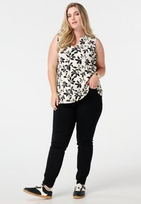 Zwart-witte bloemen mouwloze top met een v-hals, gecombineerd met zwarte slim-fit broek en zwarte sneakers met witte accenten.