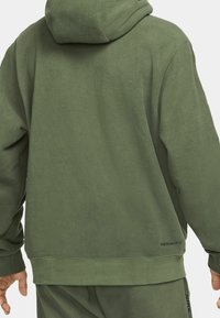 Grüne Fleece-Hoodie mit weicher Textur, ausgestattet mit einer Kapuze, gerippten Bündchen und Saum sowie einem kleinen Etikett an der unteren Seite.