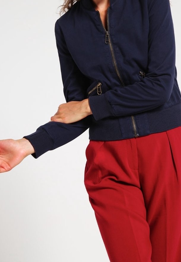 Námořnická modrá bombera s předním zipem, žebrovanými manžetami a dvěma bočními kapsami. V páru s červenými oblekovými kalhotami pro kontrast.