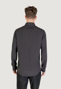 Camicia nera a maniche lunghe con bottoni, colletto classico e orlo curvato. Realizzata in tessuto liscio, presenta polsini con bottoni. Vista posteriore mostrata.