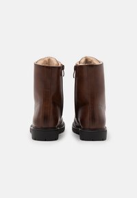 Botas de tornozelo em pele castanha com uma textura suave, bico redondo e fecho de zíper na parte de trás. Forradas com material macio para maior conforto.