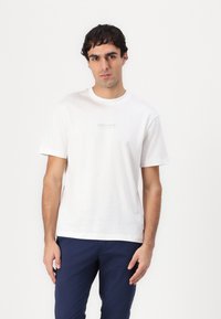 Hvid bomulds t-shirt med korte ærmer, rund hals og en lille trykt detalje på fronten, parret med marineblå bukser.