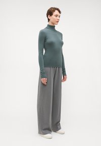 Pullover genser i skogsgrønn med en tettsittende krage; paret med vide, grå bukser og sko med hvit såle. Glatt stoff, minimalistisk design.