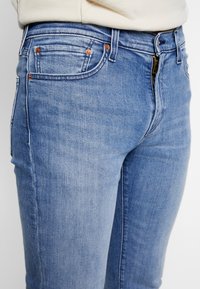 Světle modré džínové kalhoty s úzkým střihem, vybavené měděným kováním, zipem a pěti kapsami, s vybledlou texturou.