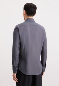 Grijze geblokte blouse met lange mouwen en een kraag, gestructureerde fit, zichtbare knopen op de manchetten en een afgeronde zoom. Glad stoftextuur.