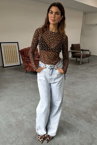 Prozirni smeđi dugi rukav s leopardskim uzorkom, uparen s svijetloplavim hlačama visokog struka i cipelama s leopardskim uzorkom, stoji unutra.