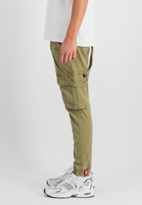 Khaki cargo nohavice so bočnými vreckami a nastaviteľnými manžetami, doplnené bielymi teniskami so sieťovinou a koženými akcentmi.