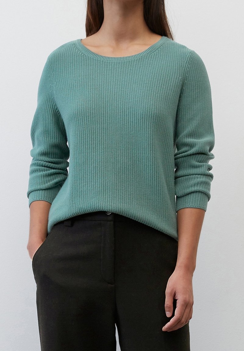 Light green ribbed knit sweater with a round neckline and long sleeves, paired with dark trousers. Texture is soft and slightly chunky.