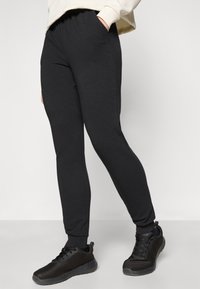 Černé tepláky s přiléhavým střihem, elastickým pasem, bočními kapsami a žebrovanými manžetami, doplněné texturovanými černými teniskami.