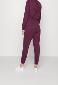 Pantaloni jogger color marrone scuro realizzati in tessuto morbido, con vita e polsini elasticizzati, abbinati a sneakers bianche.