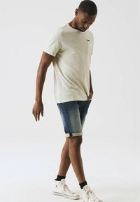 Una camiseta de manga corta gris claro con un bolsillo, combinada con unos pantalones cortos de mezclilla enrollados en los puños y zapatillas altas blancas con calcetines negros.