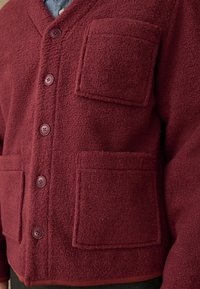 Bordeauxfarbener Fleece-Cardigan mit V-Ausschnitt, sechs Knöpfen und zwei Fronttaschen. Texturiert, lockere Passform und kontrastierendes Saumdetail.
