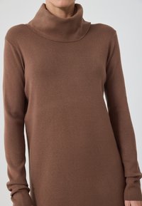 Pulover cu guler înalt, ribetat, de culoare maro, cu maneci lungi si o croiala lejera. Textură moale, design minimalist și detaliu cu guler înalt.