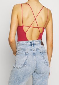 Ribbad bodysuit i burgundy med djup rygg och korsade remmar, i kombination med högmidjade ljusblå denimjeans med bakfickor.