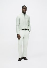 Πουκάμισο με πράσινες και λευκές ρίγες και κουμπιά, ανοιχτόχρωμο παντελόνι, μαύρη ζώνη και καφέ παπούτσια. Απαλό ύφασμα, άνετη εφαρμογή και casual σχεδίαση.