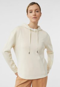 Felpa color crema con cappuccio e lacci, maniche lunghe e vestibilità rilassata. Tessuto morbido e dettagli di design minimi, abbinata a pantaloni beige.