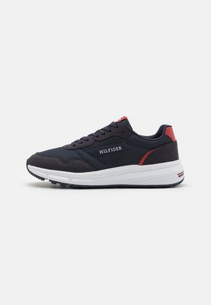 Navy sneaker with white sole, featuring red accents. Fabric upper with reinforced heel, lace-up design, and branded detailing on the side.
