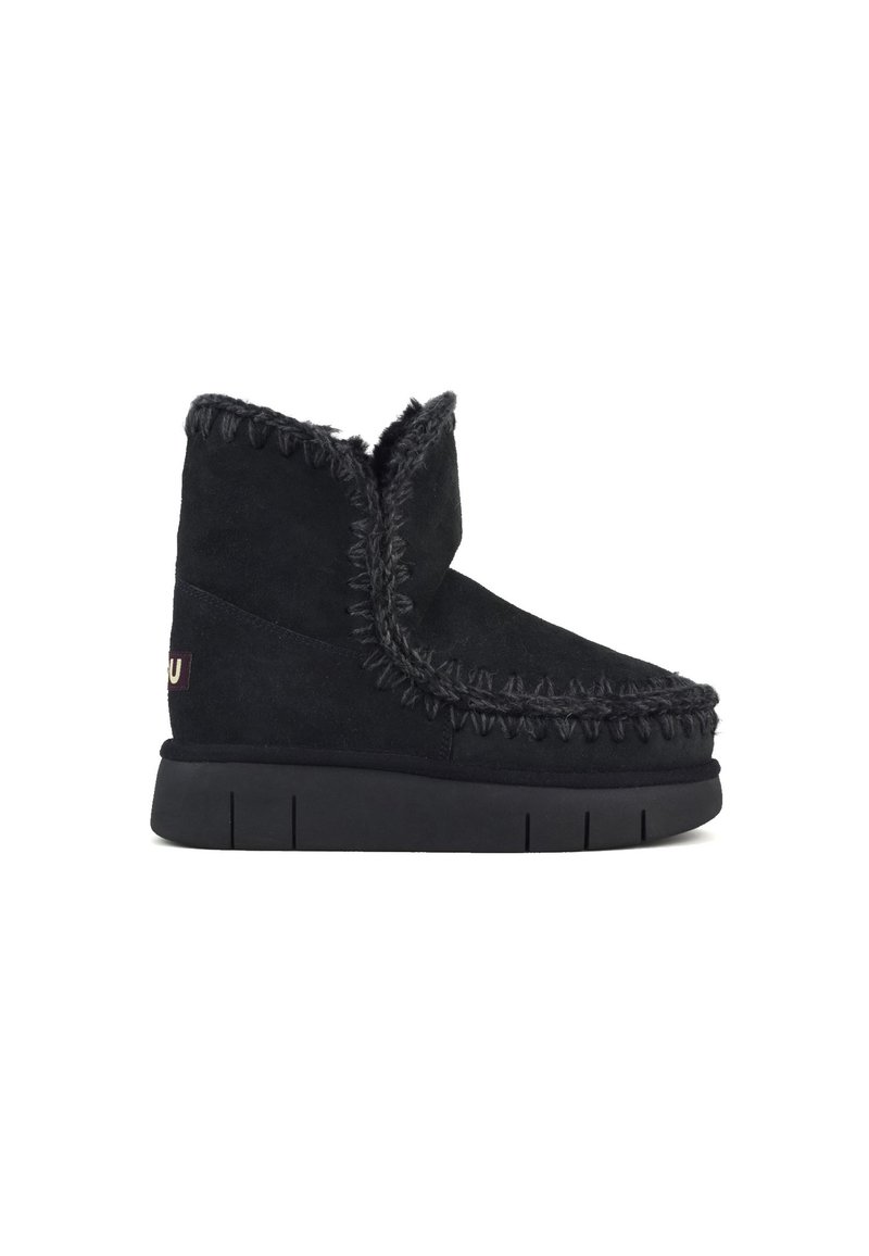 Stivale alla caviglia in suede nero con suola spessa, caratterizzato da cuciture decorative e un interno in tessuto morbido. Inclusa etichetta con logo laterale.