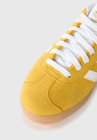 Geel suede sport schoen met witte veters en accenten. Beschikt over een ronde neus en een gumrubberen zool, met een gestructureerd bovenwerk.
