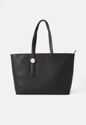 Borsa tote nera in pelle con superficie testurizzata, due manici lunghi e un accento circolare in argento su un cinturino verticale.