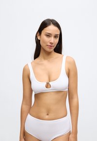Λευκό ριμπ τοπ μπικίνι με φαρδιές τιράντες, λαιμόκοψη scoop και κεντρικό κυκλικό άνοιγμα με μεταλλική διακόσμηση. Συνδυάζεται με ταιριαστό σλιπ ψηλόμεσο.