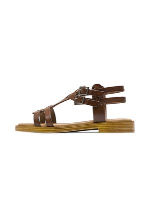 Sandalia plana de cuero marrón con múltiples correas y dos hebillas metálicas ajustables en una suela con textura de madera.