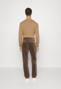 Pantalon en velours marron à coupe décontractée, associé à un haut beige à manches longues et cintré. Le modèle porte des baskets blanches.