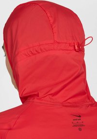 Haut à capuche léger rouge avec une capuche resserrée, présentant des détails de couture et une petite étiquette dans le dos, fabriqué à partir d'un matériau lisse et durable.
