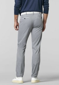 Hellgraue Hose mit schmalem Schnitt, flachem Bund und zwei Gesäßtaschen. Getragen mit einem weißen gewebten Gürtel und weißen Sneakers, die eine glatte Oberfläche aufweisen.