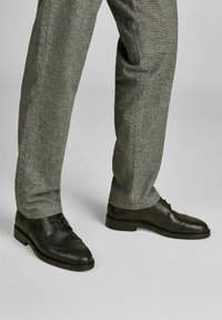 Schwarze Leder-Brogues mit durchbrochenen Details, kombiniert mit grauen strukturierten Hosen, die ein klassisches, niedriges Design und eine Schnürung zeigen.