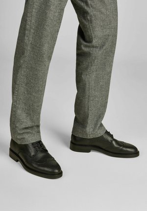 Schwarze Leder-Brogues mit durchbrochenen Details, kombiniert mit grauen strukturierten Hosen, die ein klassisches, niedriges Design und eine Schnürung zeigen.