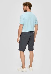 Chemise à manches courtes bleu clair associée à un short gris foncé. Le short a des poches et une coupe décontractée, complété par des baskets blanches.