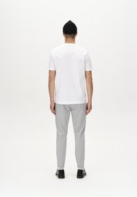 Vit bomullströja, avslappnad passform, i kombination med grå tapered byxor och svarta skor. Enkel design, minimal detaljering, slät textur.