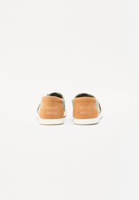 Zapatillas marrones y verdes con parte superior de ante y tela, que cuentan con una suela blanca, un diseño minimalista y un logo en el talón.