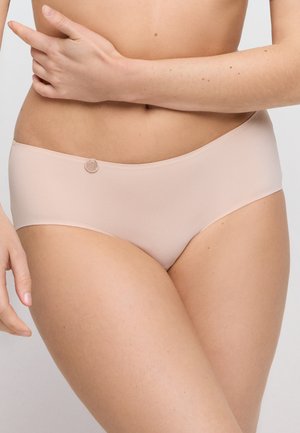 Femme portant un sous-vêtement hipster couleur chair sans couture, bras croisés sur le ventre, sur fond uni.