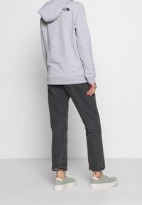 Sudadera gris con un logo en la parte trasera, detalles negros, combinada con pantalones gris oscuro y zapatillas verde claro, con tejido texturizado y un corte relajado.