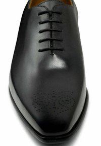 Zwart leren geklede schoen met een gladde textuur, puntige neus en zes oogjes voor de veters. Heeft geperforeerde details op het teengedeelte.