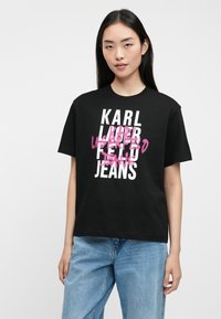 T-shirt preto de algodão com texto em branco ousado e acentos em estilo graffiti rosa. Combinado com jeans de denim azul claro, com um corte descontraído.