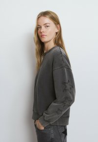 Sudadera gris fabricada en una mezcla de algodón, con apliques de estrellas texturizadas en las mangas, puños y dobladillo acanalados, y un ajuste relajado.