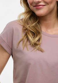 T-shirt rose clair avec des manches courtes retroussées et un col rond. Tissu doux et lisse ; design minimal sans motifs ou accents visibles.
